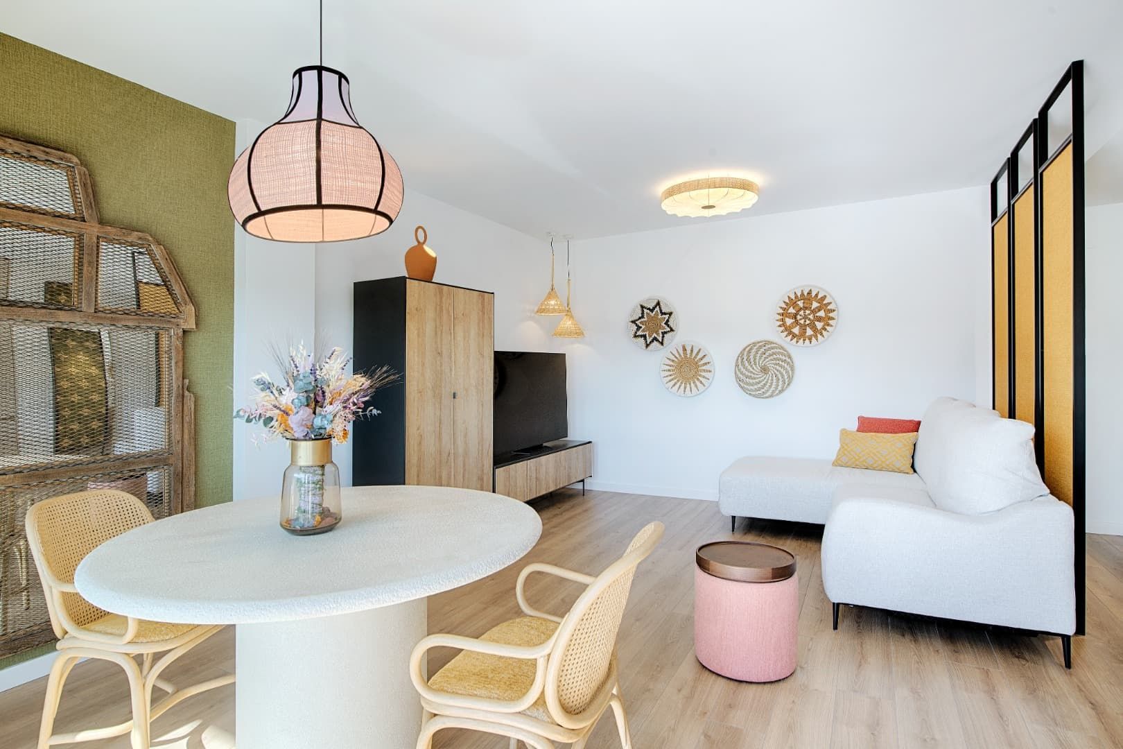 Luminoso salón-comedor moderno con sofá blanco, mesa redonda, sillas de mimbre y detalles en madera clara.