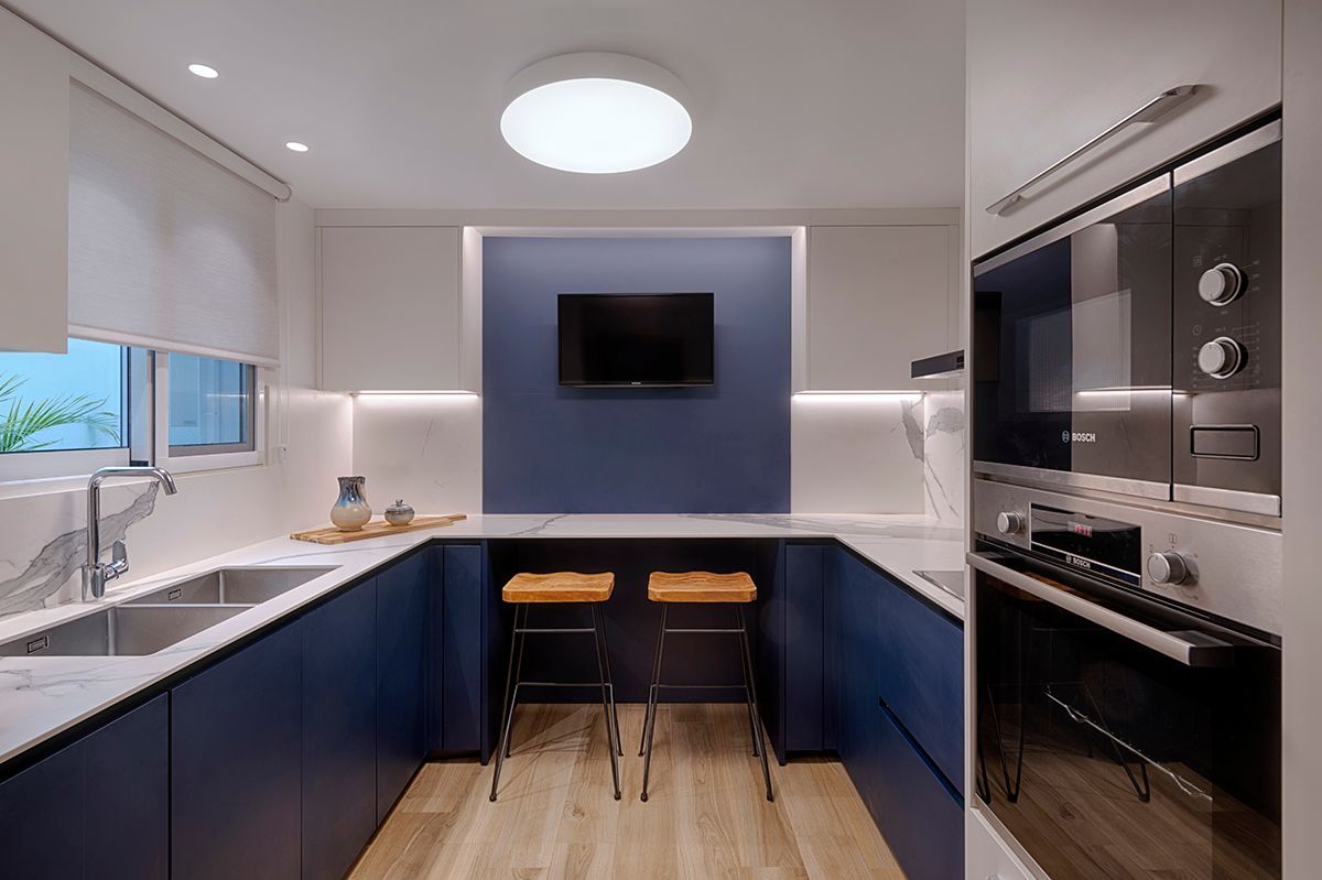 Una cocina con gabinetes azules, un fregadero, una estufa y un televisor.