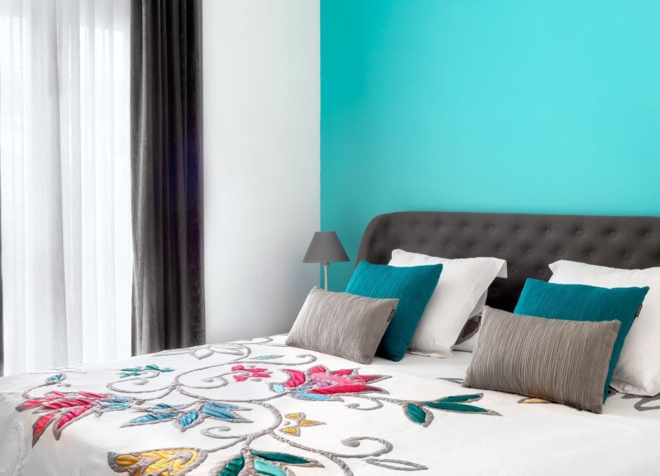 Un dormitorio con una cama, almohadas, una lámpara y una pared azul.