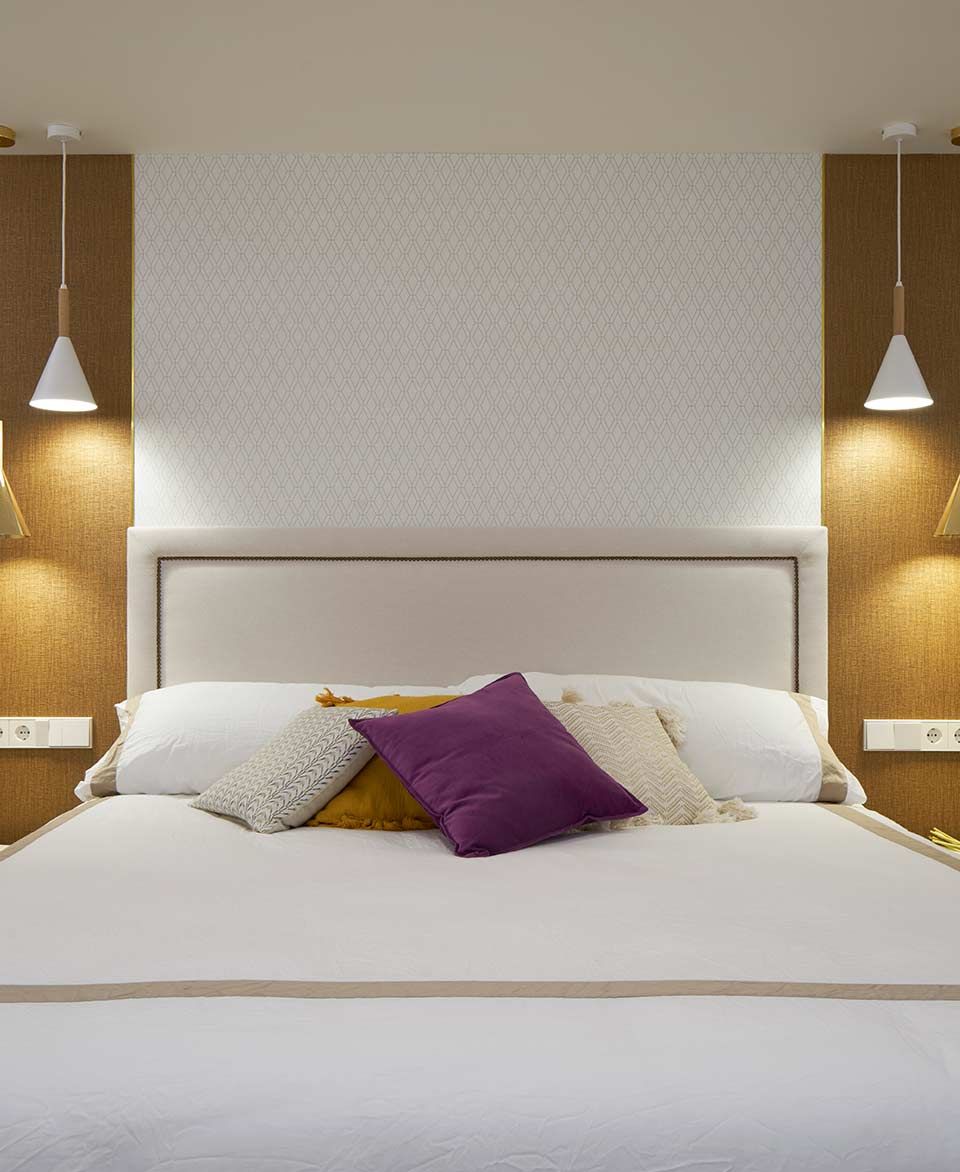 Una cama con sábanas blancas y almohadas moradas en un dormitorio.