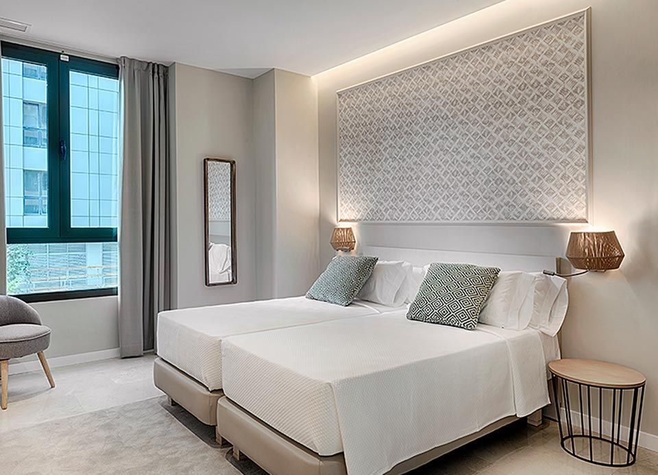 Una habitación de hotel con dos camas, una silla y un espejo.