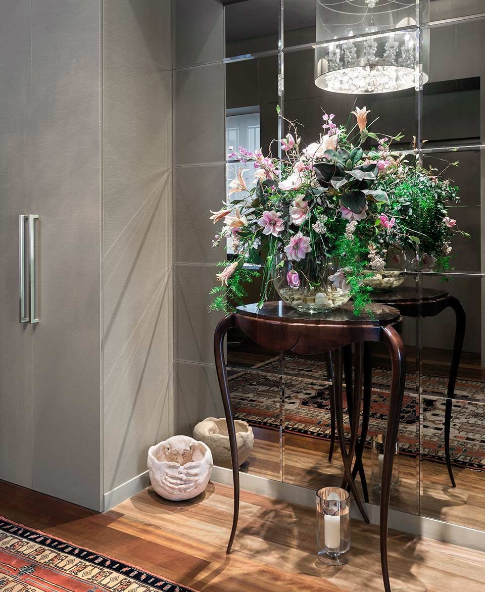 Un jarrón de flores reposa sobre una mesa frente a un espejo.