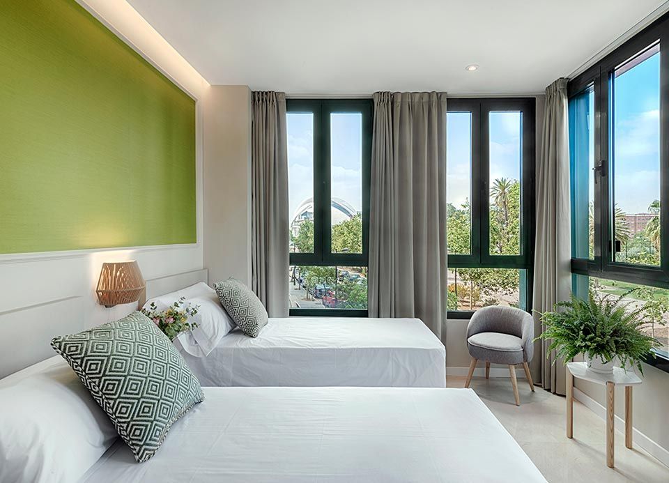 Una habitación de hotel con dos camas, una silla y una ventana grande.