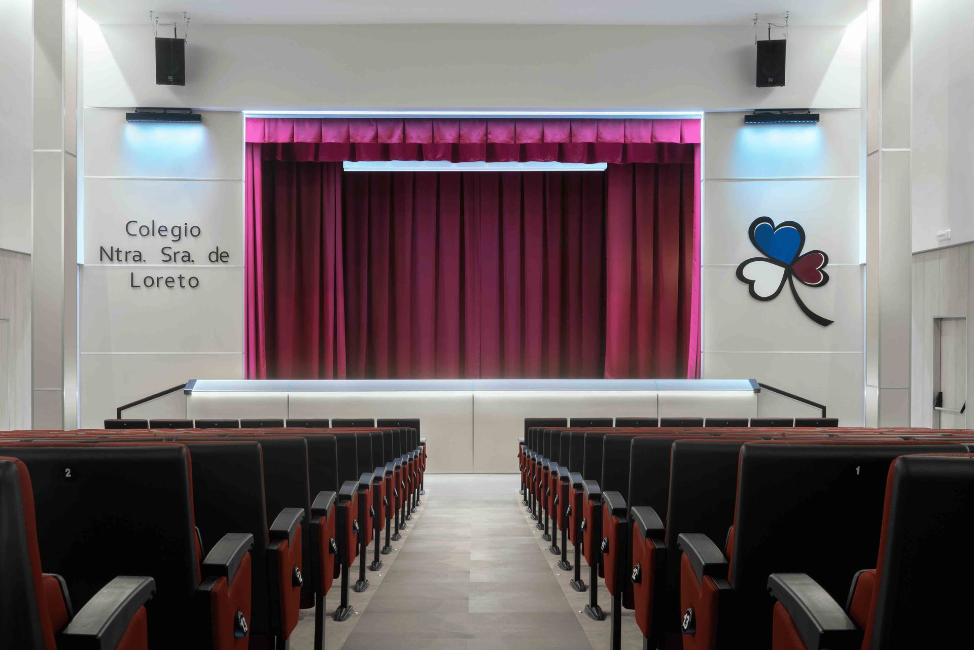 Un auditorio con filas de asientos y un escenario con una cortina roja.