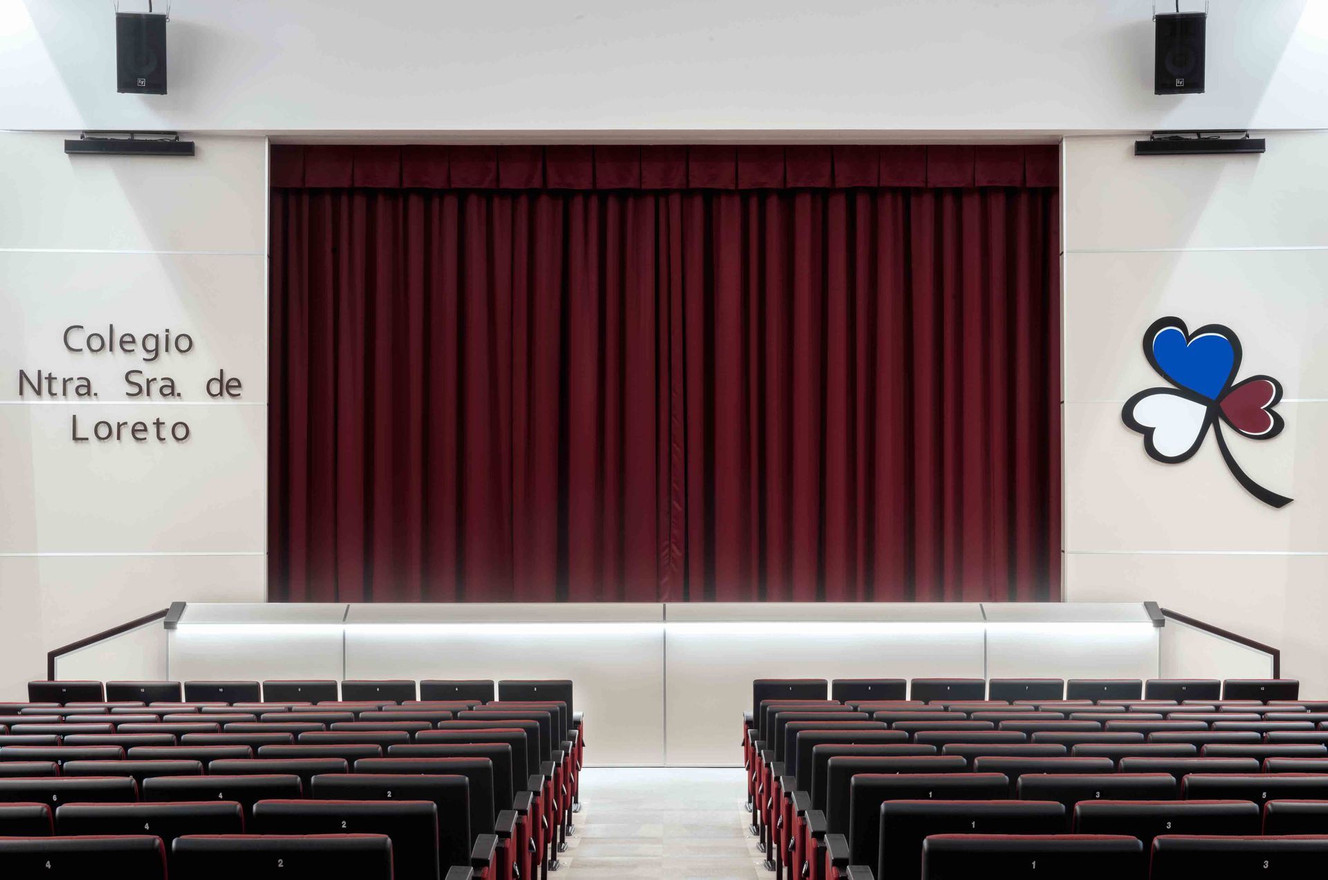 Un auditorio con filas de asientos y una cortina roja que dice colegio