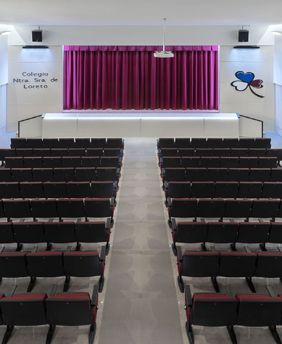 Un auditorio con filas de asientos y un escenario con una cortina morada.