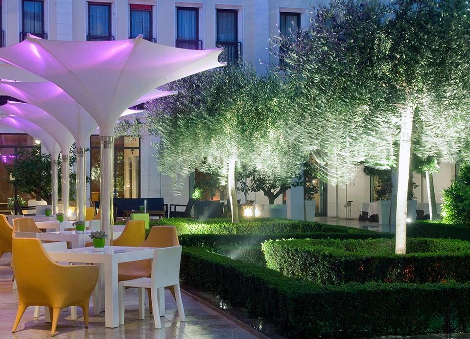 Una fila de mesas y sillas bajo sombrillas moradas en un jardín.