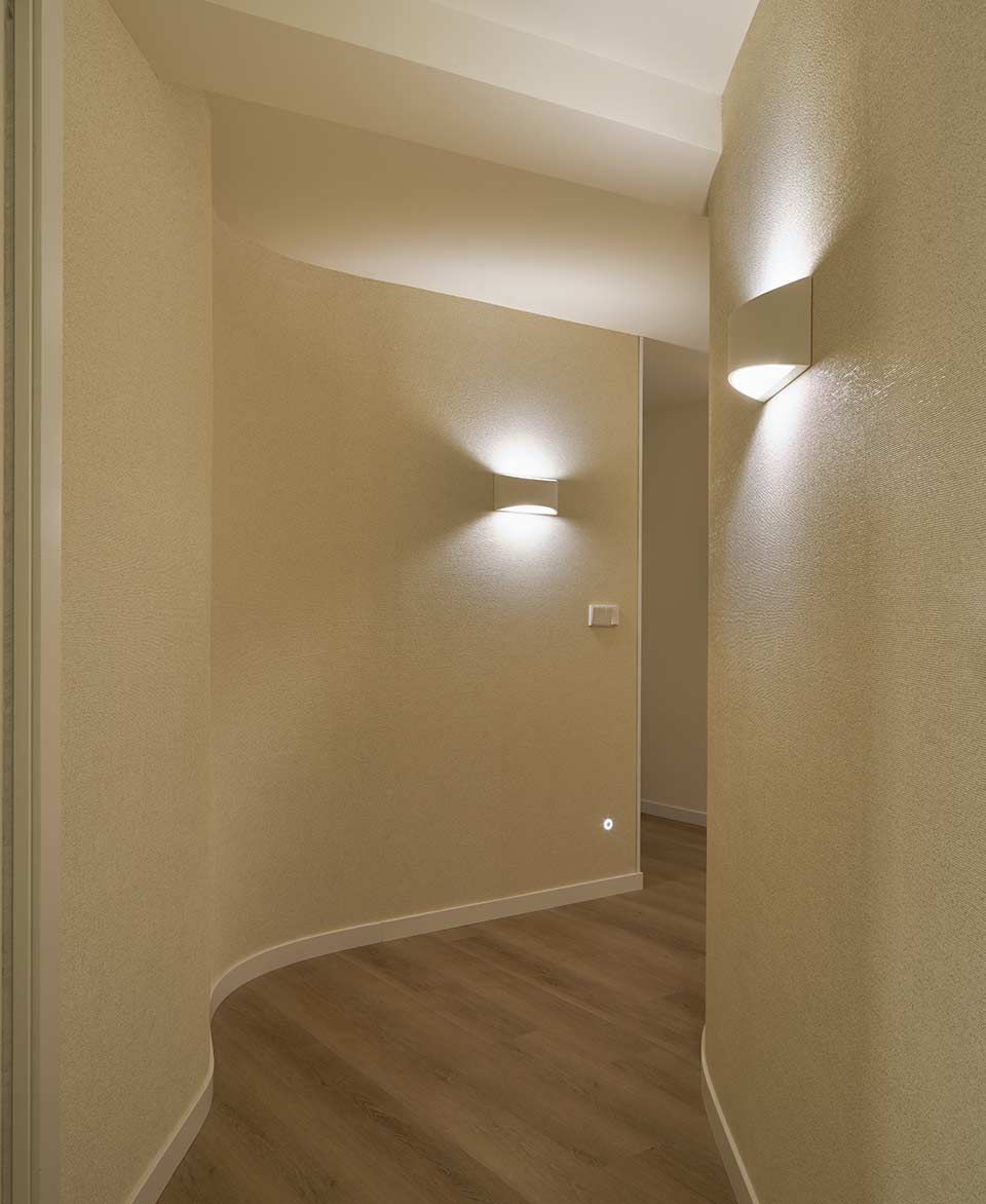 Un pasillo con suelo de madera y dos luces en la pared.