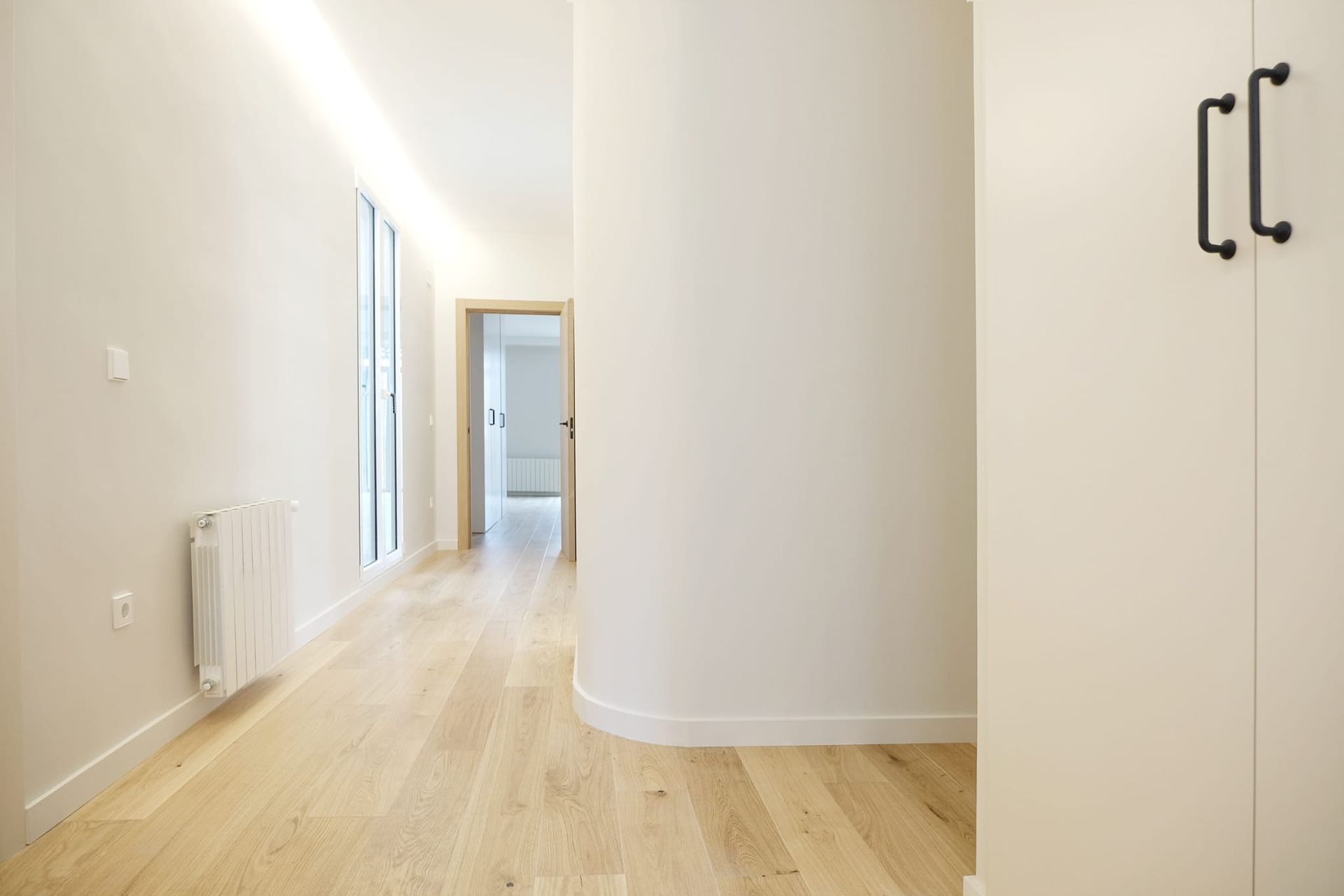 Un pasillo vacío con pisos de madera y paredes blancas.