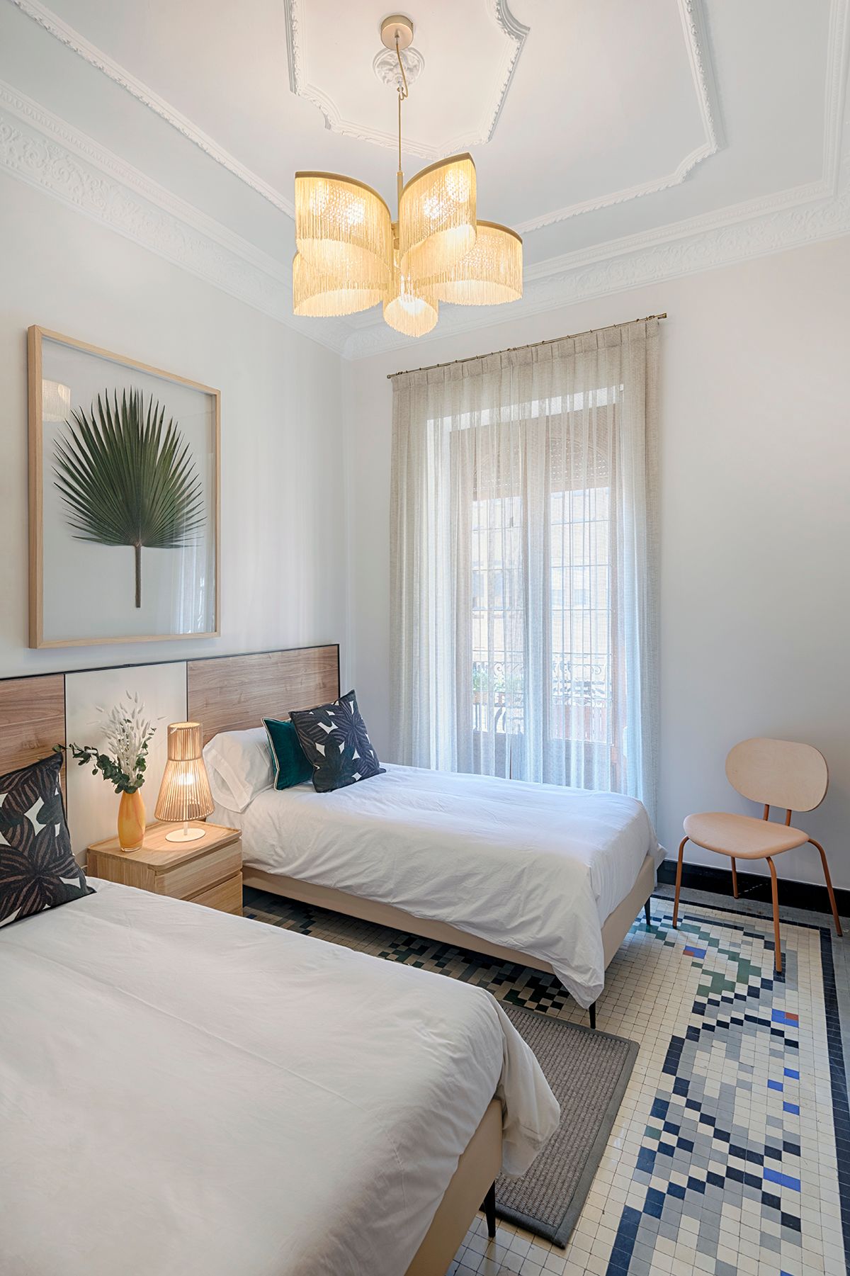 Un dormitorio con dos camas, una silla, una alfombra y una lámpara de araña.