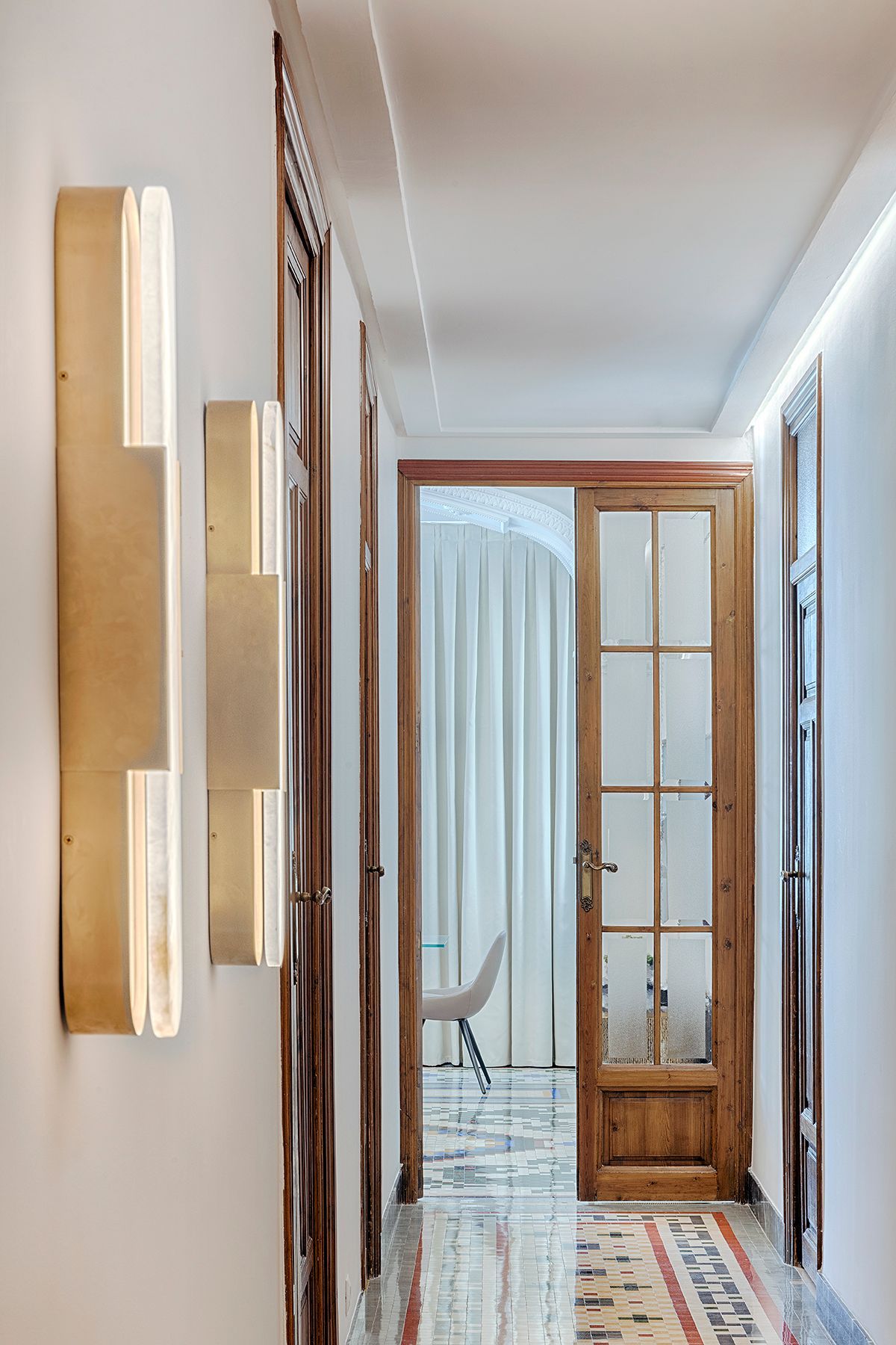 Un pasillo largo con una puerta de madera y dos luces en la pared.