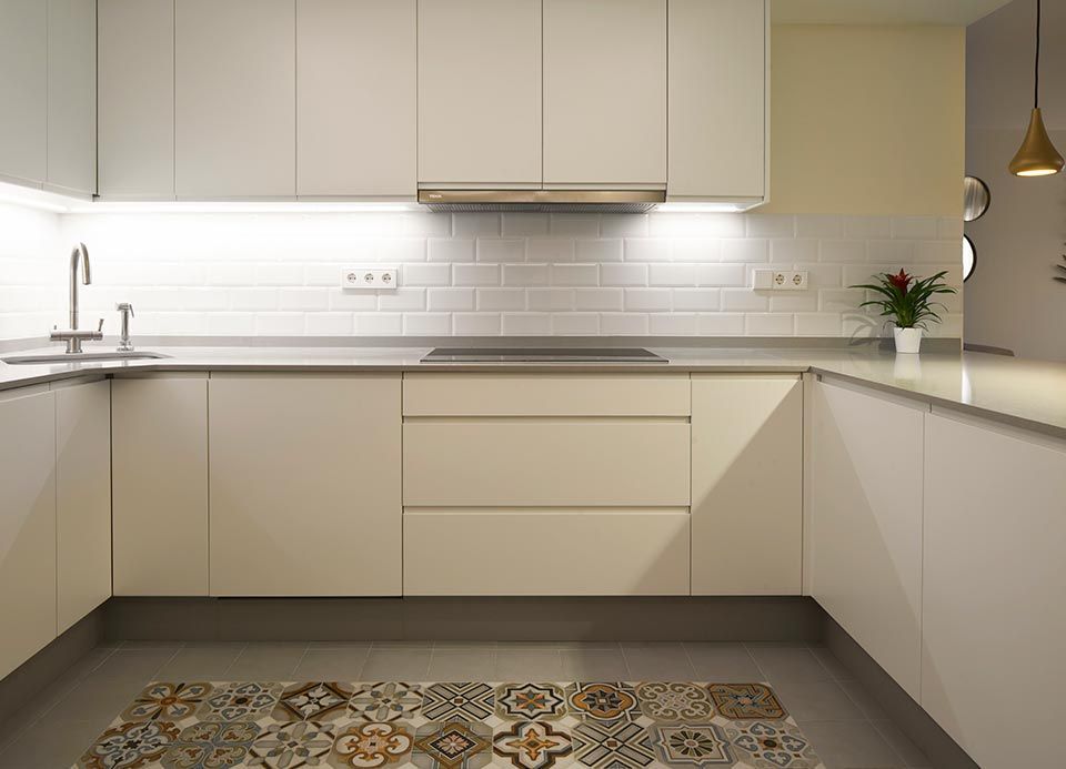 Una cocina con gabinetes blancos, una estufa, un fregadero y una alfombra en el piso.