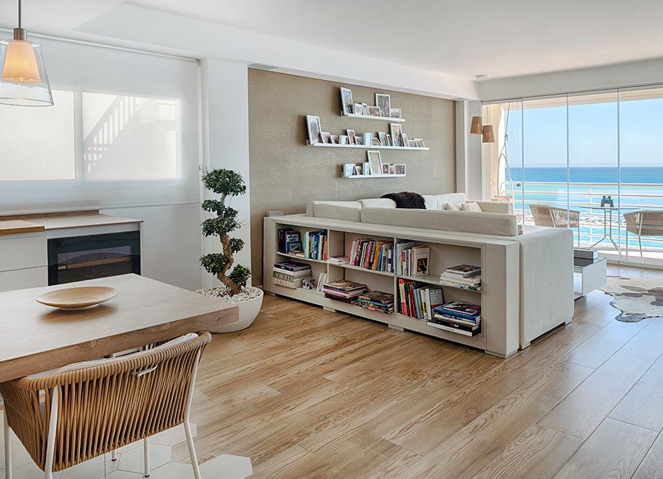 Una sala de estar con sofá, mesa, sillas, estantería y vista al océano.