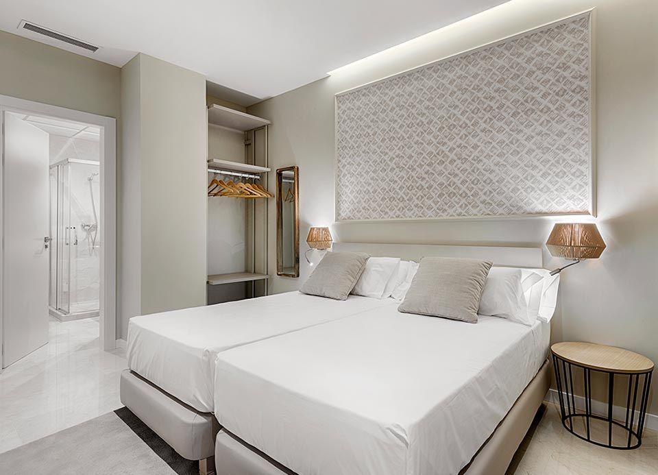 Una habitación de hotel con dos camas, una mesita de noche y un espejo.