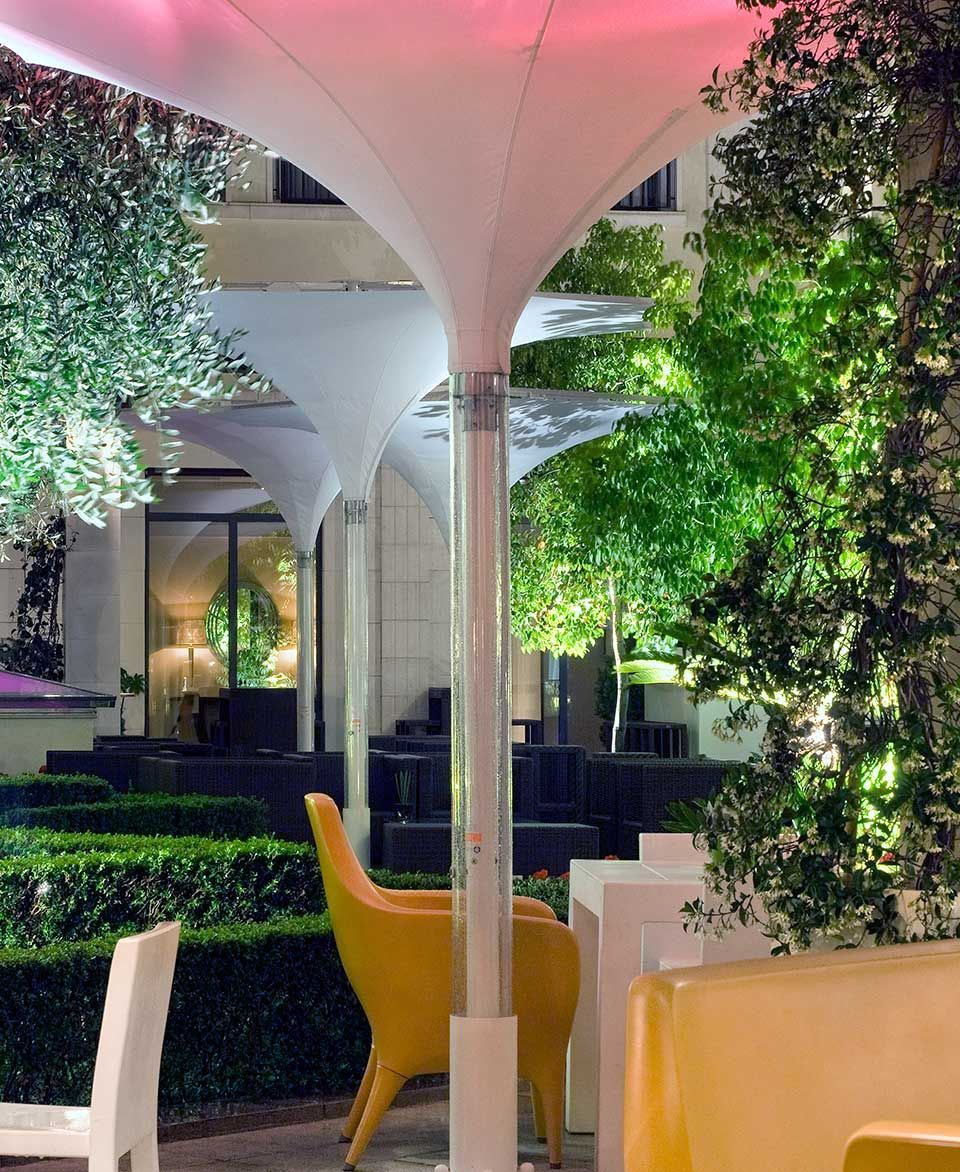 Un patio con sillas y mesas bajo una sombrilla rosa.