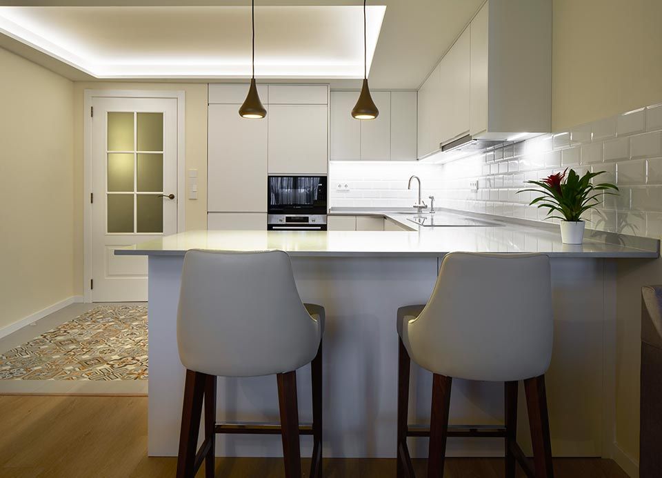 Una cocina con gabinetes y taburetes blancos y una planta en la encimera.