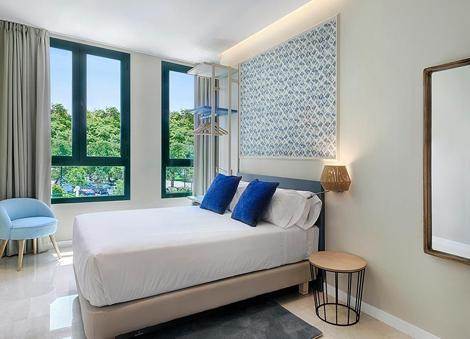 Una habitación de hotel con una cama king size, dos ventanas, una mesa y un espejo.