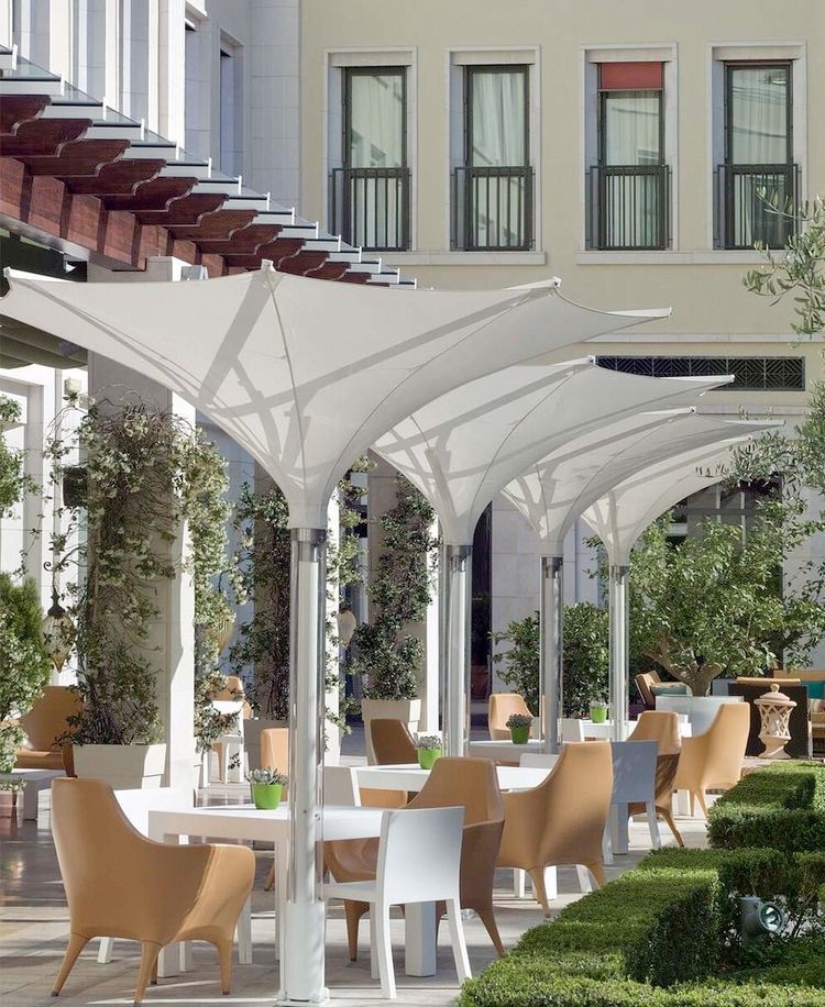 Mesas y sillas bajo sombrillas blancas frente a un edificio