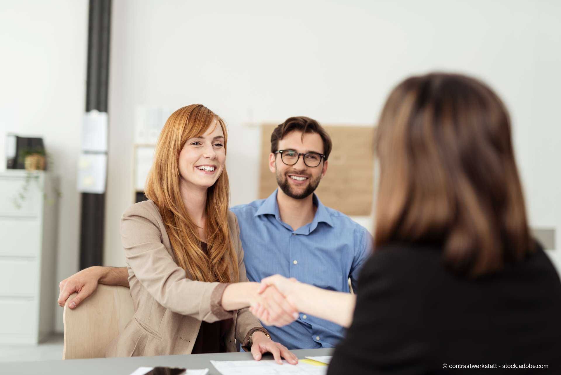 glückliches paar schüttelt beraterin die hand

