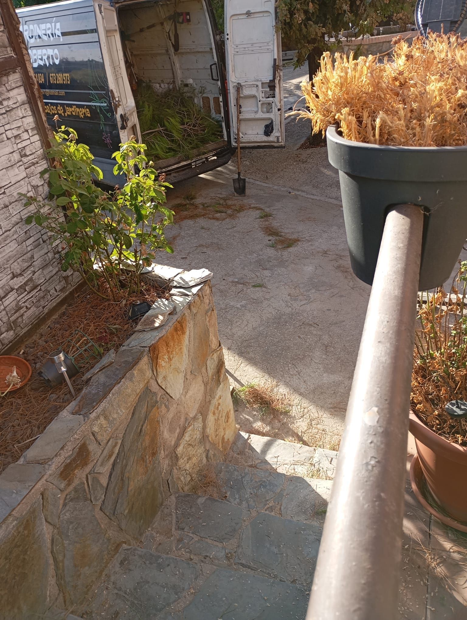 Un camión de reparto estacionado cerca de un jardín con plantas y muros de piedra.