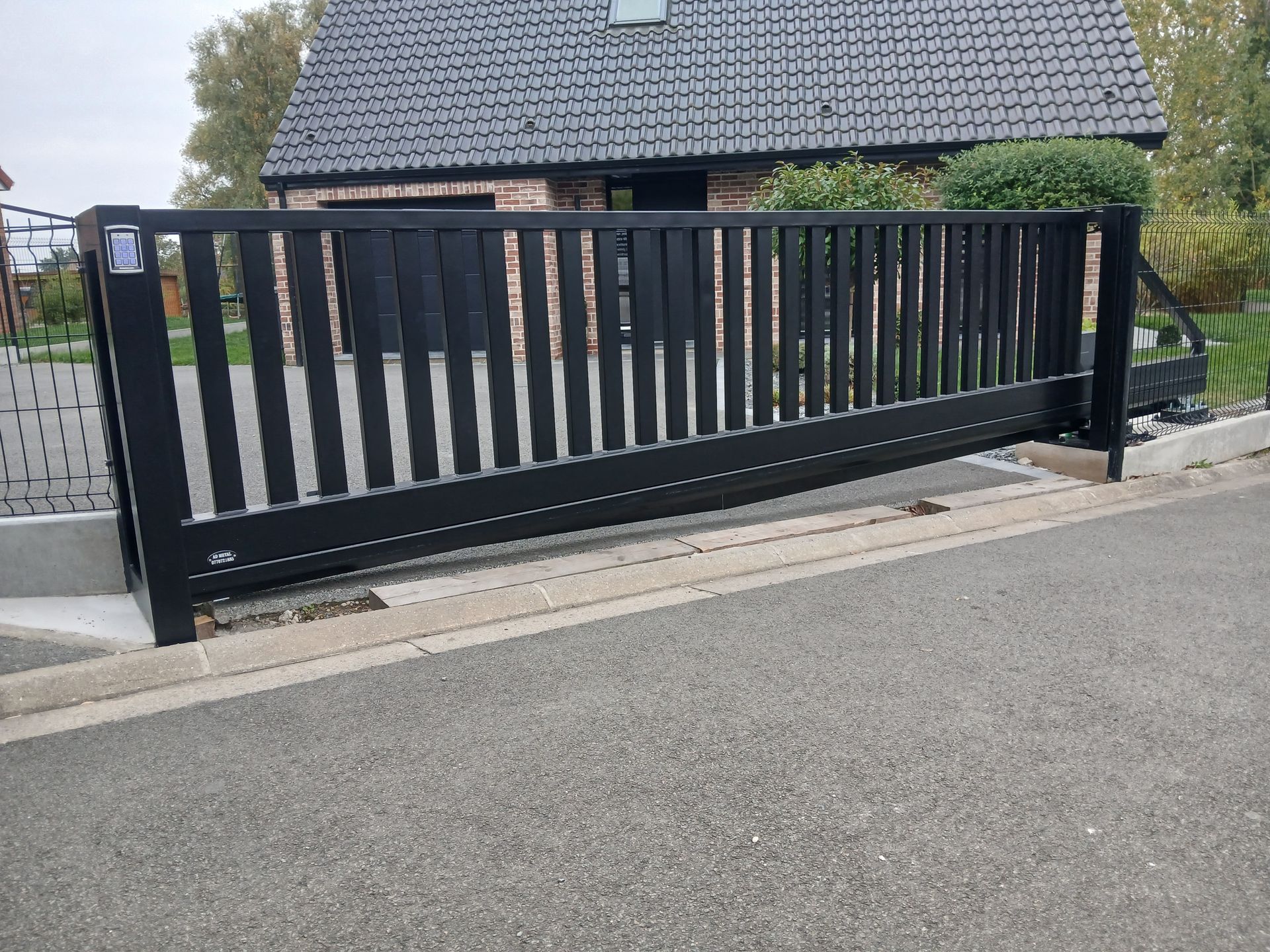 Portail coulissant noir devant une maison en briques, sur une allée pavée.