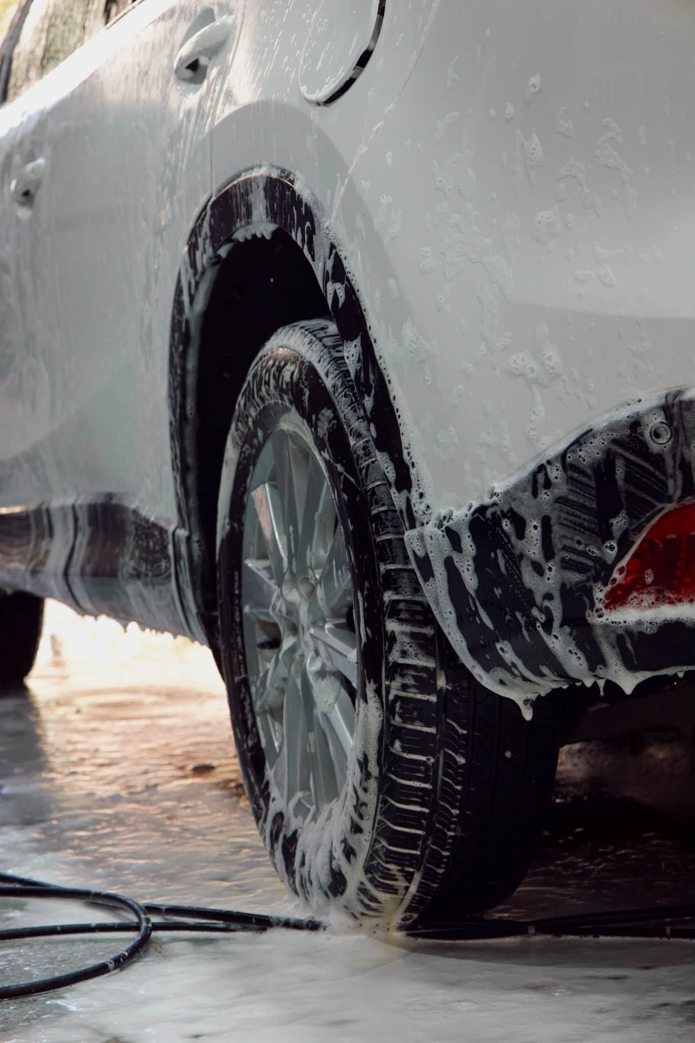Un neumático de coche siendo lavado con agua y jabón, en primer plano sobre un pavimento mojado.