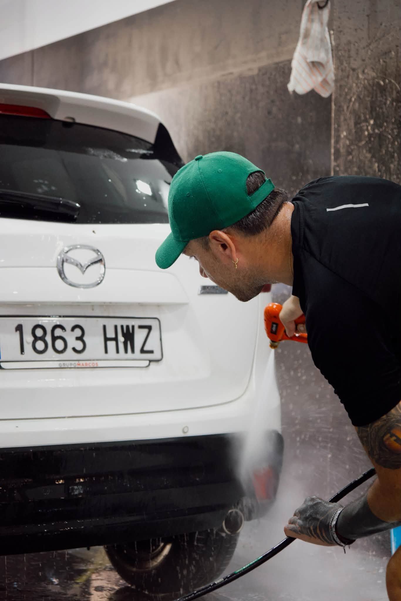 Hombre lavando un SUV Mazda blanco con una hidrolimpiadora en un lavado de coches