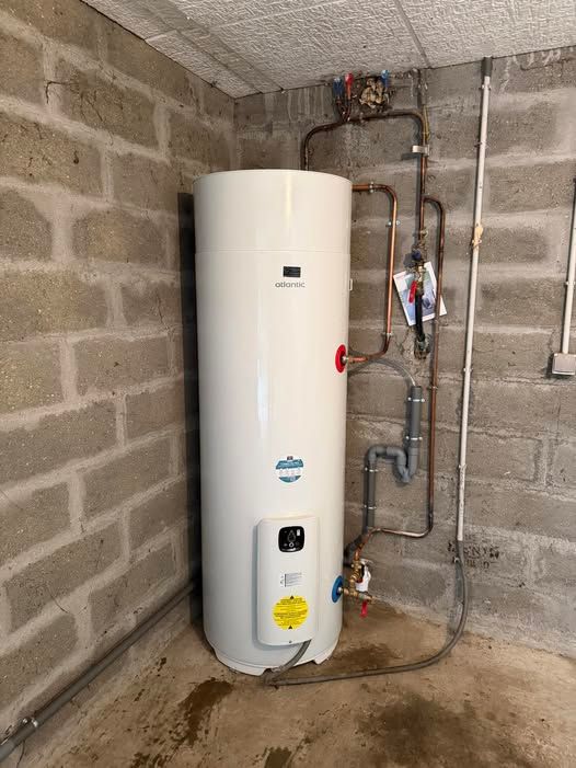 Chauffe-eau blanc dans une buanderie en parpaings avec tuyauterie apparente et sol en béton