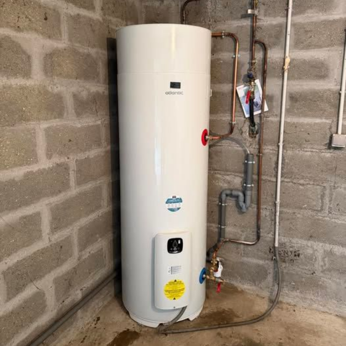 Chauffe-eau cylindrique blanc avec tuyaux apparents dans une buanderie en briques.