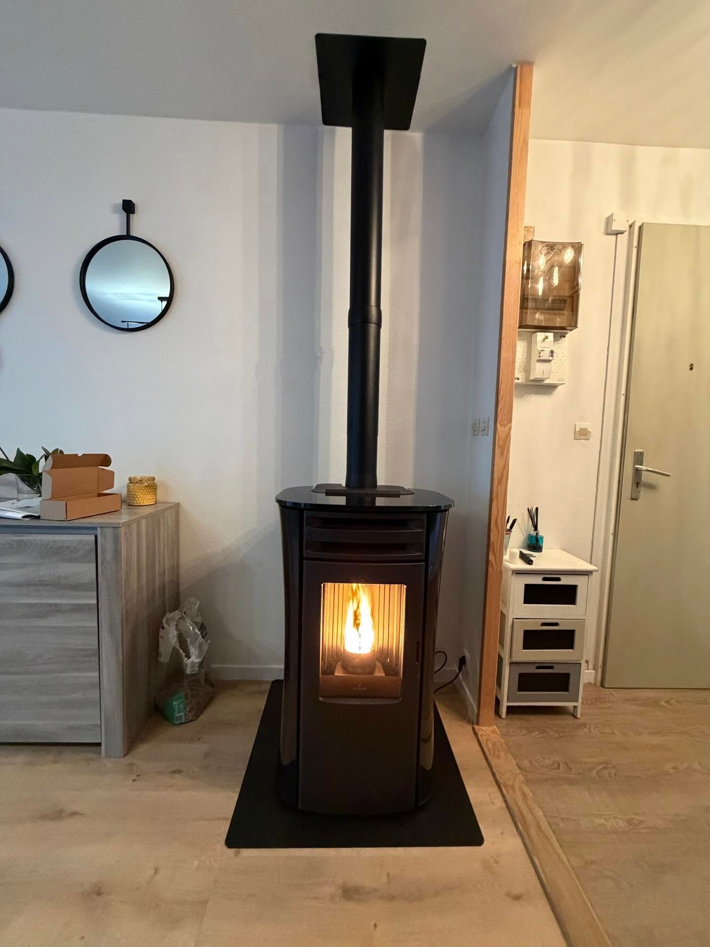 Poêle à bois noir brûlant dans un salon aux murs clairs et à proximité d'une porte