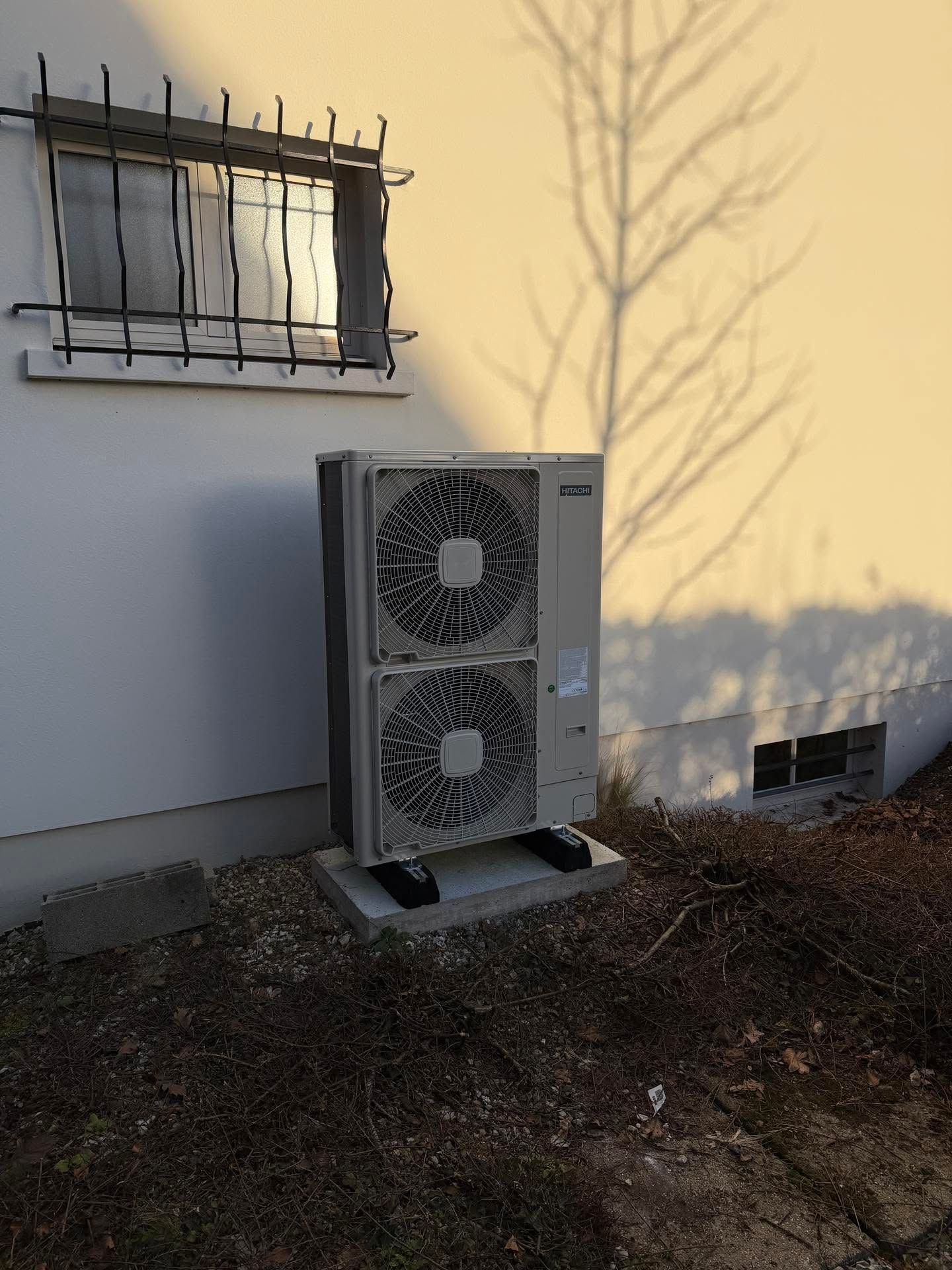 Unité de pompe à chaleur extérieure adossée à un mur beige d'une maison