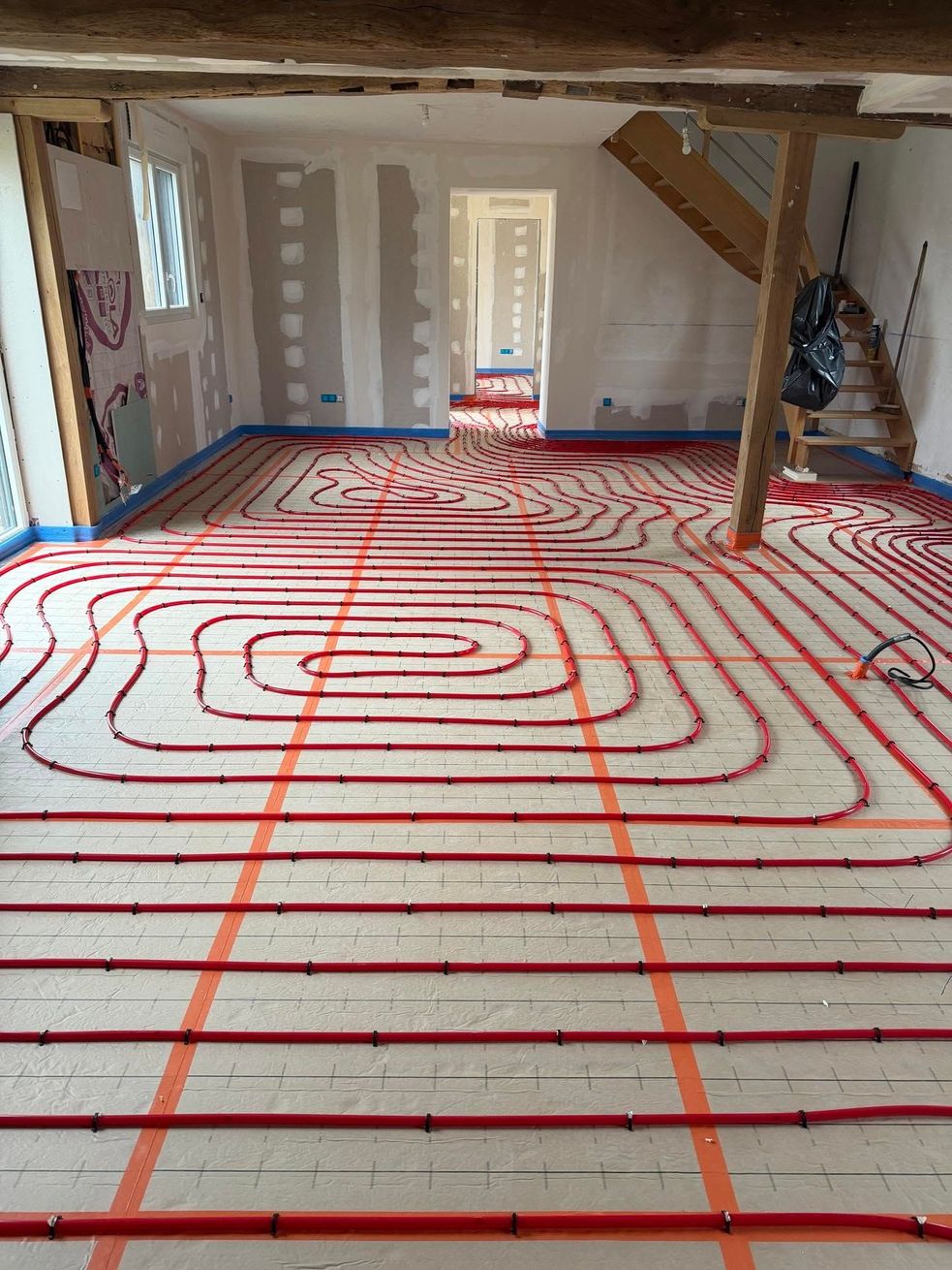 Pièce intérieure en rénovation avec des tuyaux de chauffage au sol rouges posés sur un plancher en contreplaqué.