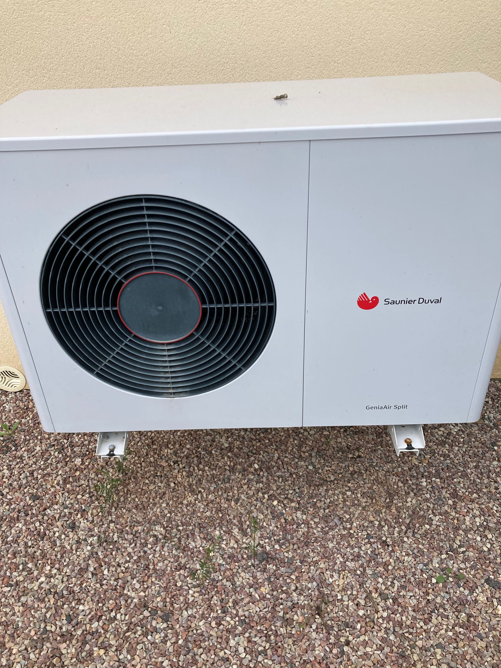 Unité de climatisation extérieure blanche avec un grand ventilateur noir, posée sur une surface de gravier.