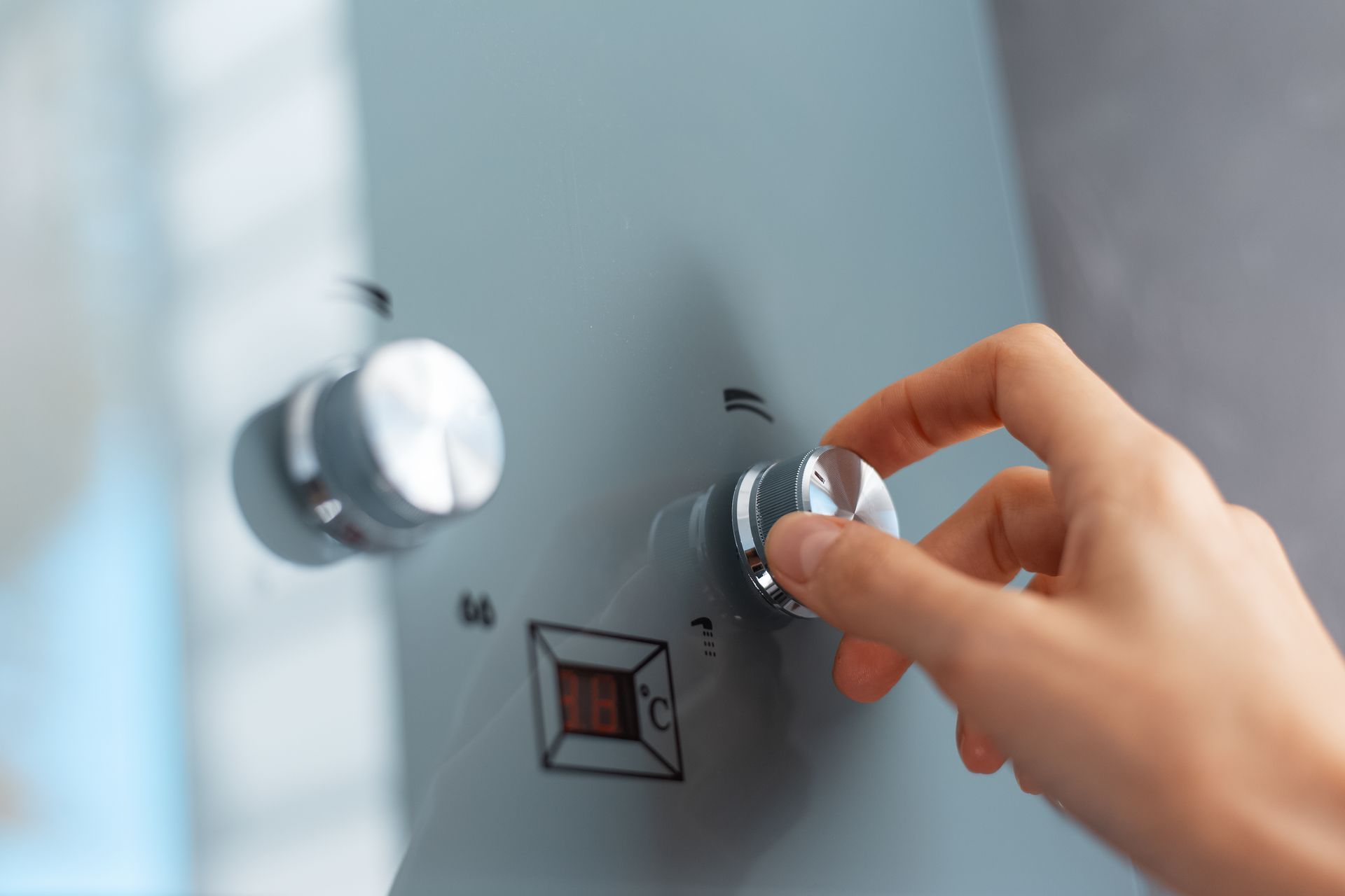 Une main tournant un bouton de commande de douche argenté sur un panneau mural gris