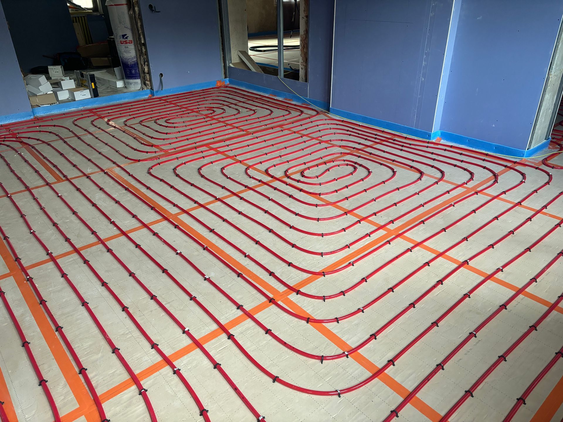 Pièce intérieure en rénovation avec des tuyaux de chauffage au sol rouges posés sur des panneaux isolants.