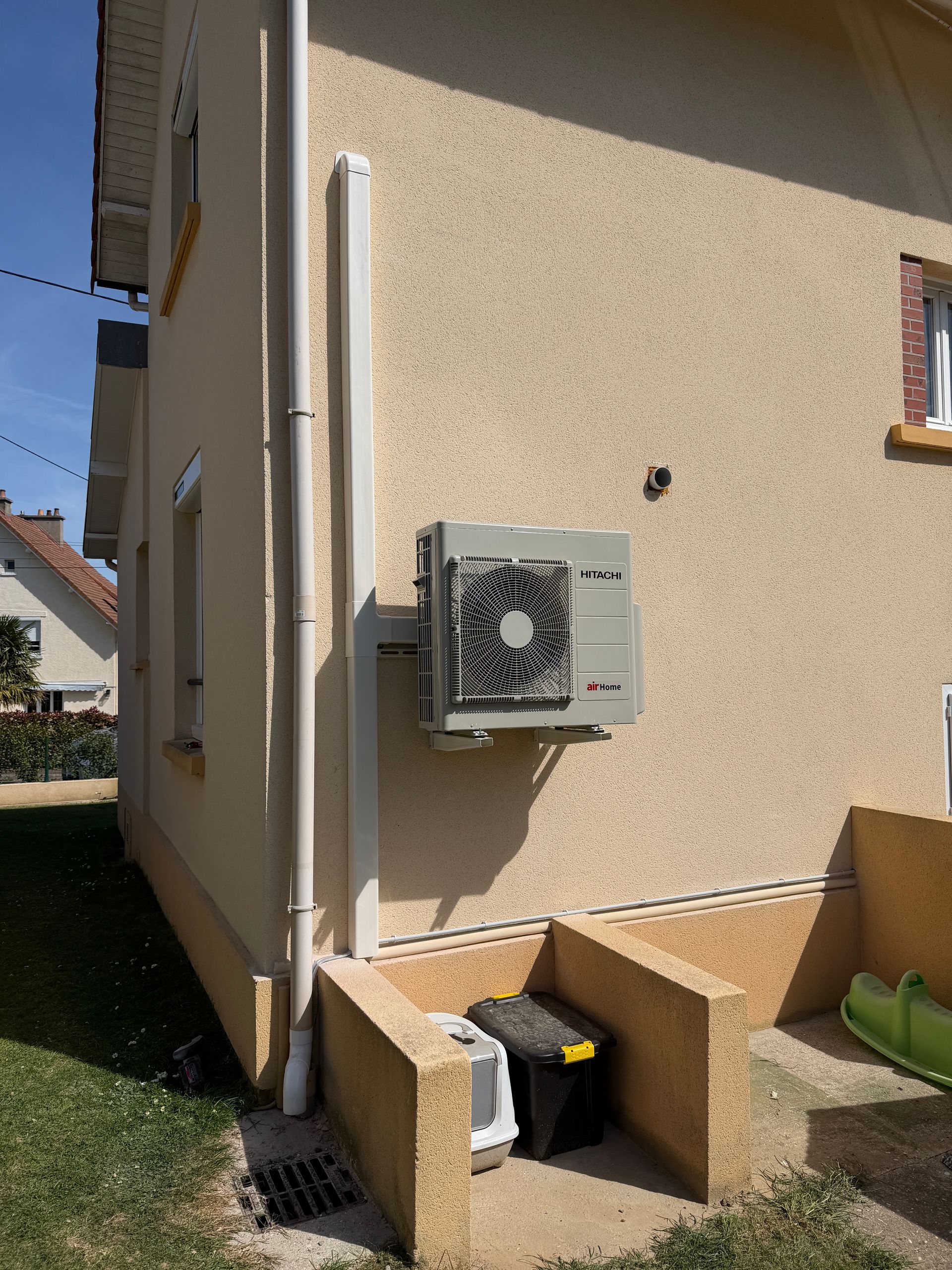 Mur extérieur de la maison avec un climatiseur mural et des boîtiers techniques à côté d'une petite ouverture