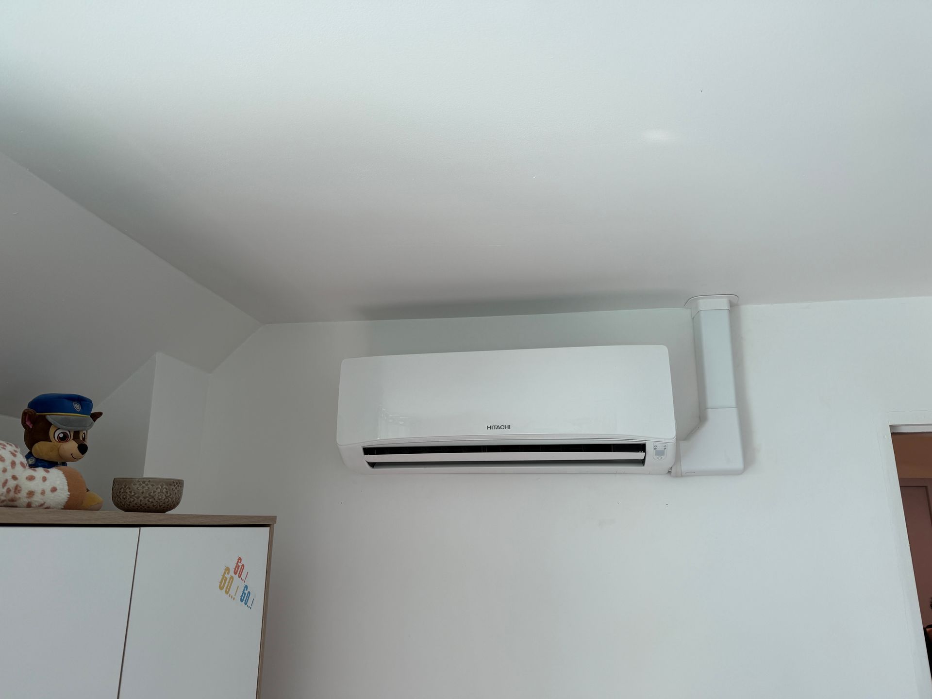 Climatiseur mural blanc au-dessus d'une armoire dans un coin lumineux d'une pièce.