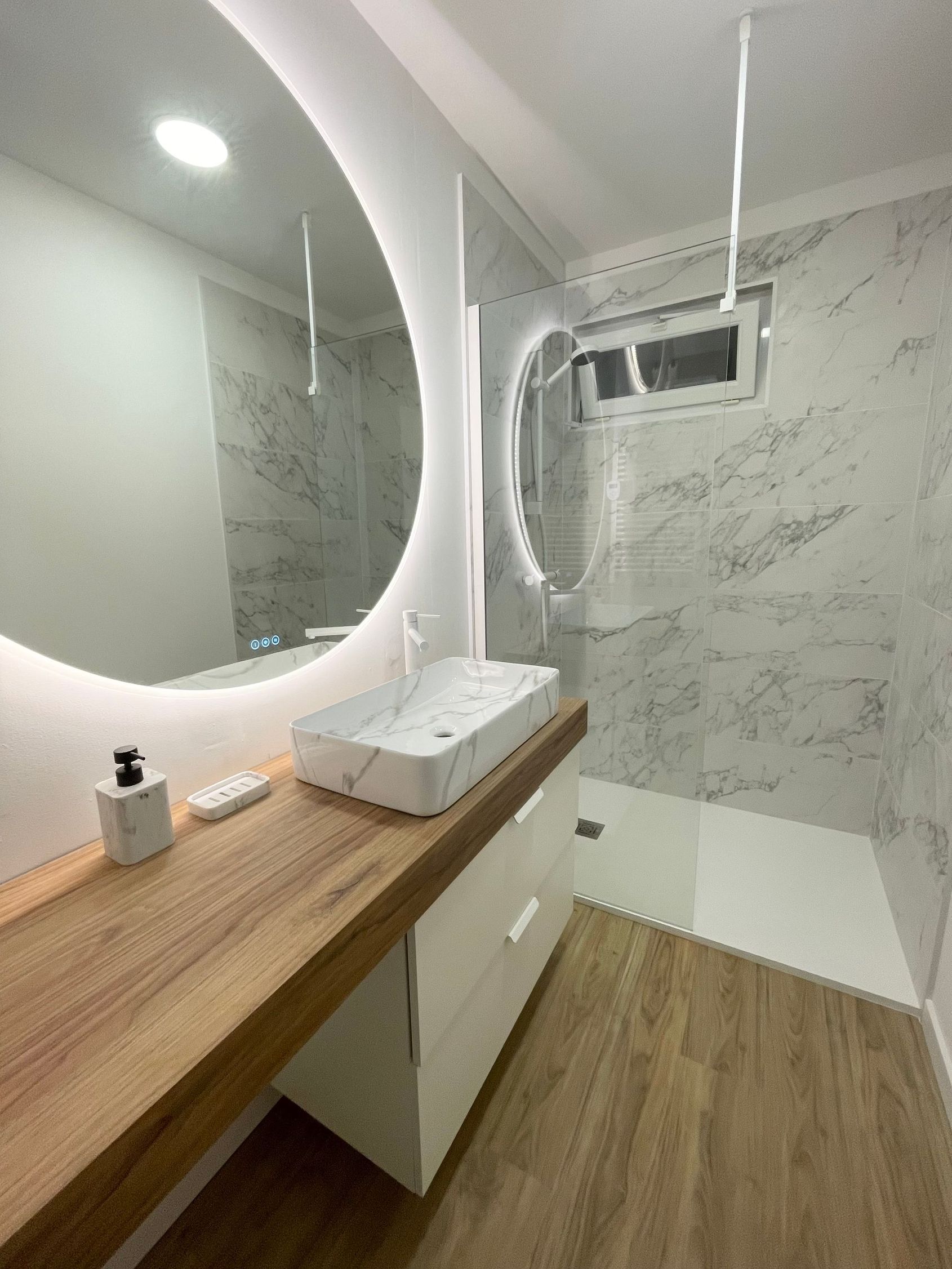 Meuble-lavabo moderne avec comptoir en bois, miroir rond et murs carrelés à motif marbre