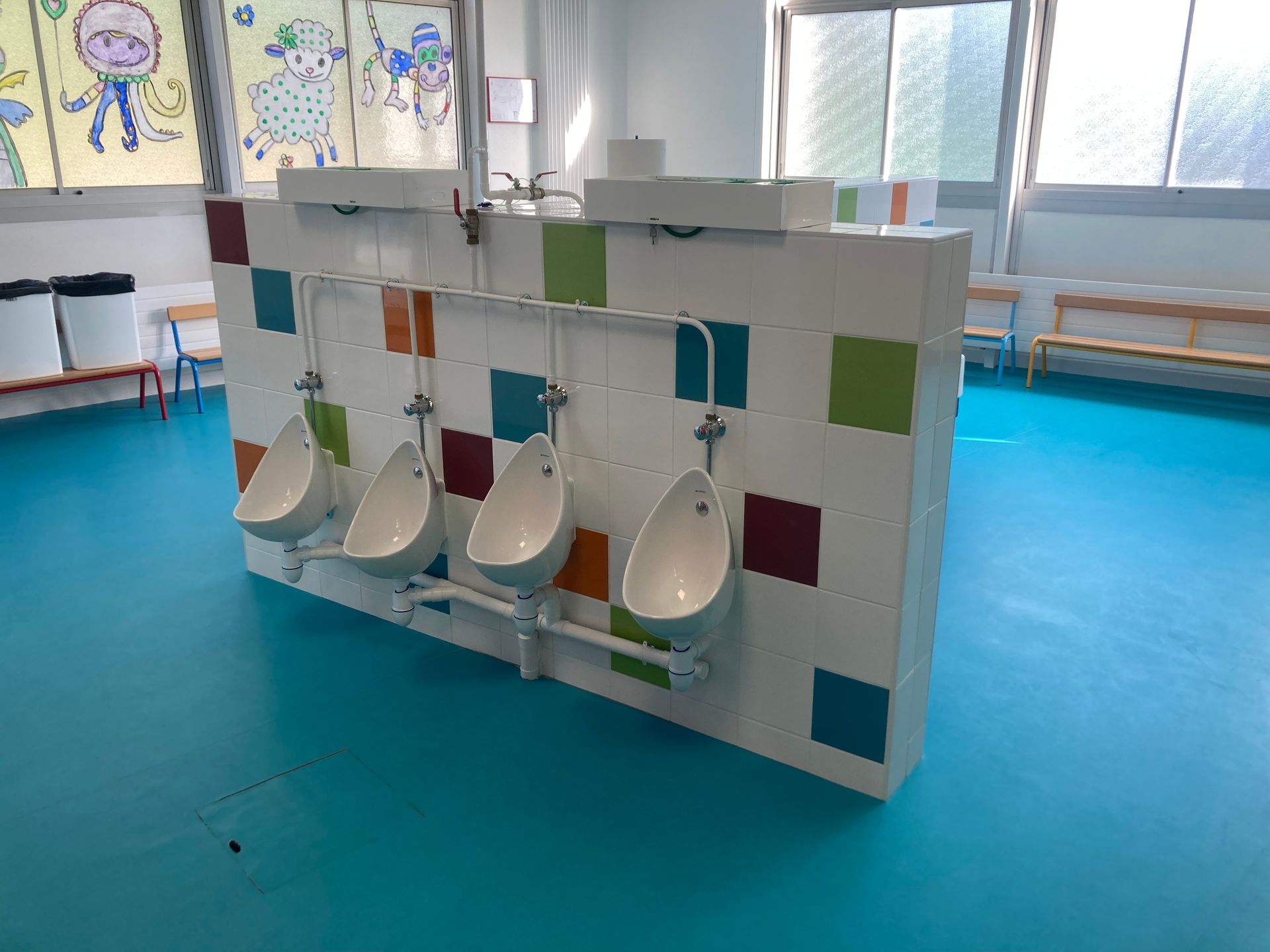 Des urinoirs blancs sur un mur carrelé dans des toilettes au sol bleu vif.