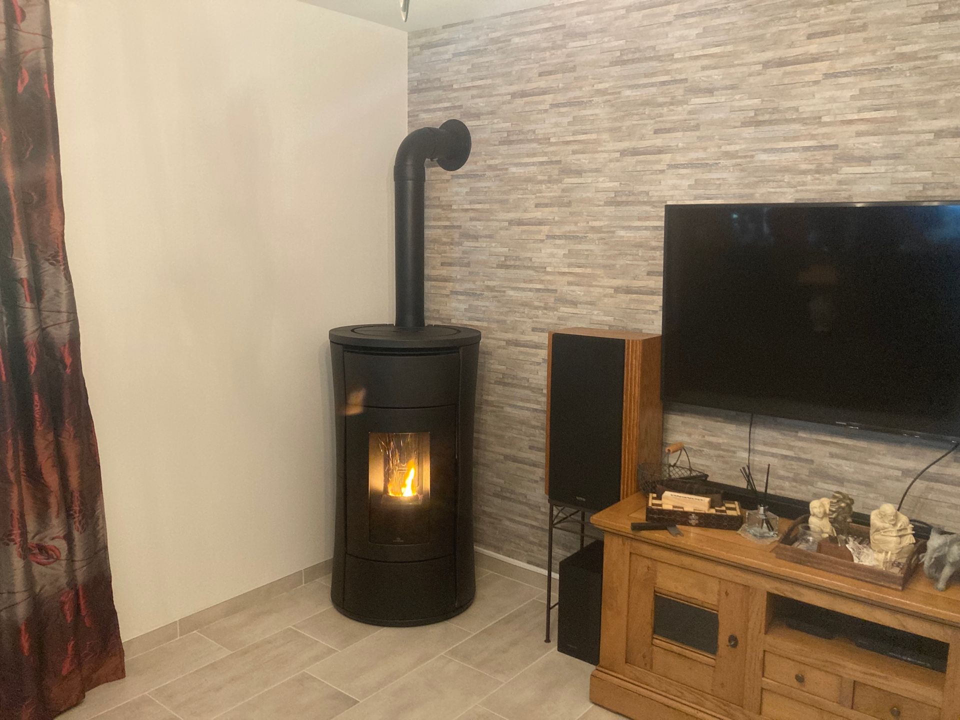 Salon avec un poêle à bois noir allumé à côté d'une télévision et d'un meuble TV en bois.