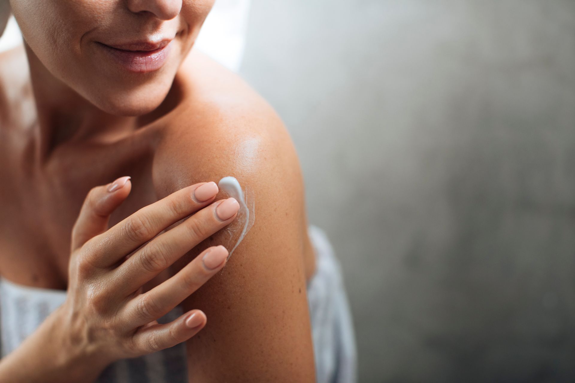 Une personne applique de la lotion sur son épaule à l'aide d'un coton, gros plan sur peau nue.