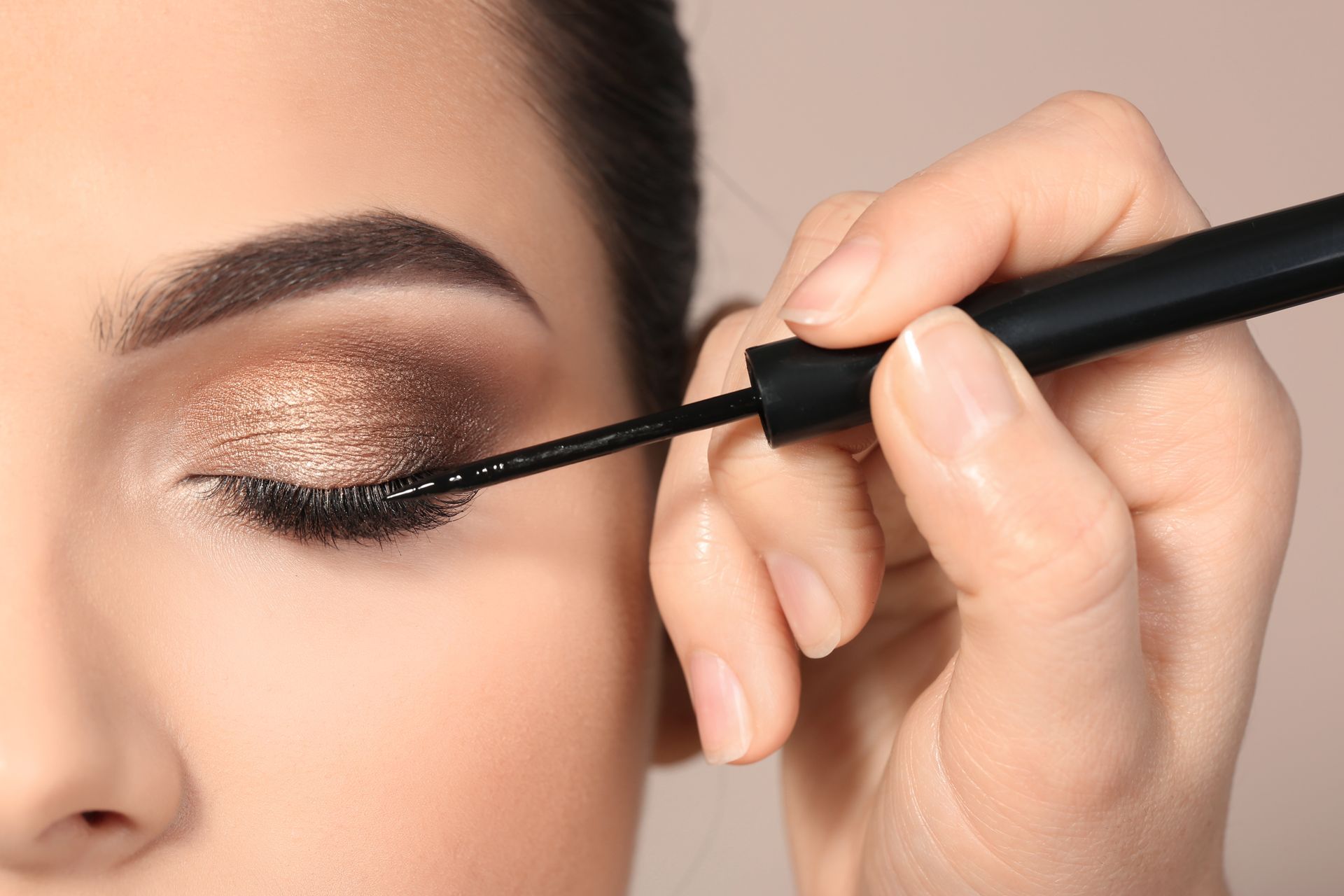 Gros plan sur un œil maquillé avec un eye-liner liquide noir et un fard à paupières cuivré scintillant.