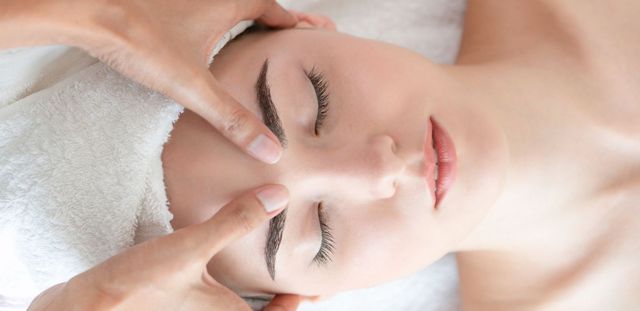 Gros plan sur une femme allongée, les yeux fermés, pendant un massage du visage ou un soin spa.