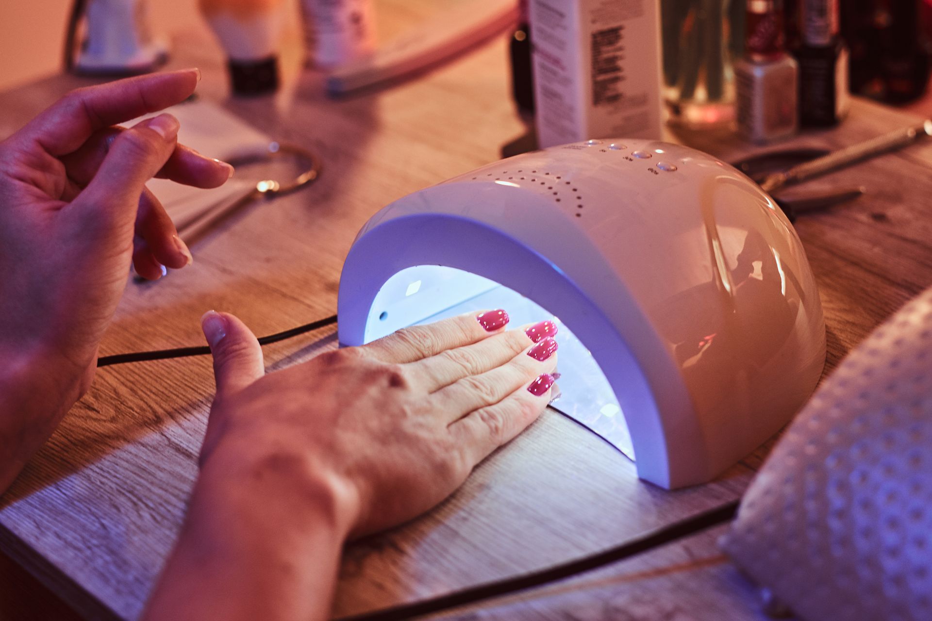 Main sous une lampe UV blanche pour le séchage d'une manucure sur une table en bois.