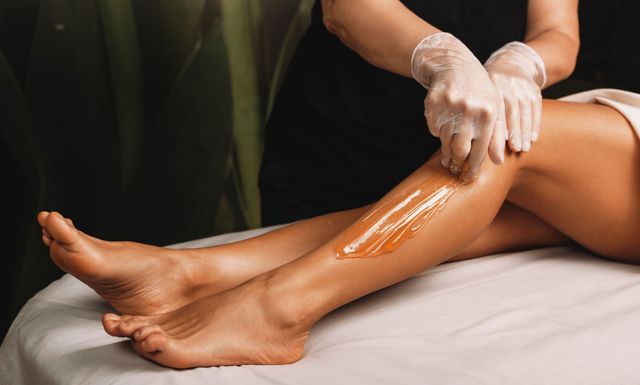 Une esthéticienne applique de l'huile de massage sur la jambe d'une cliente allongée sur une table de soin.