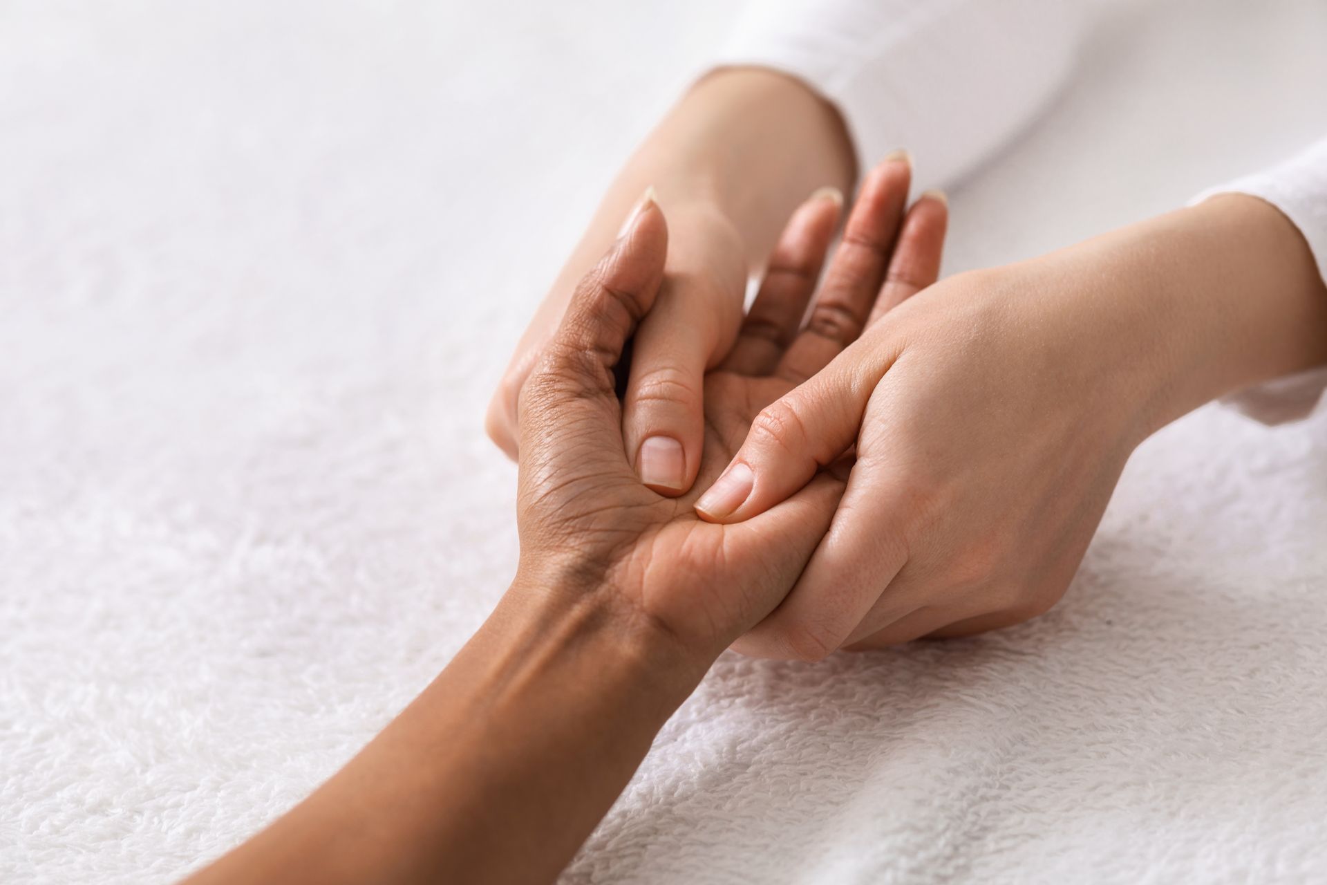 Des mains tenant délicatement un poignet posé sur une serviette blanche, suggérant un massage ou une séance de thérapie réconfortante.