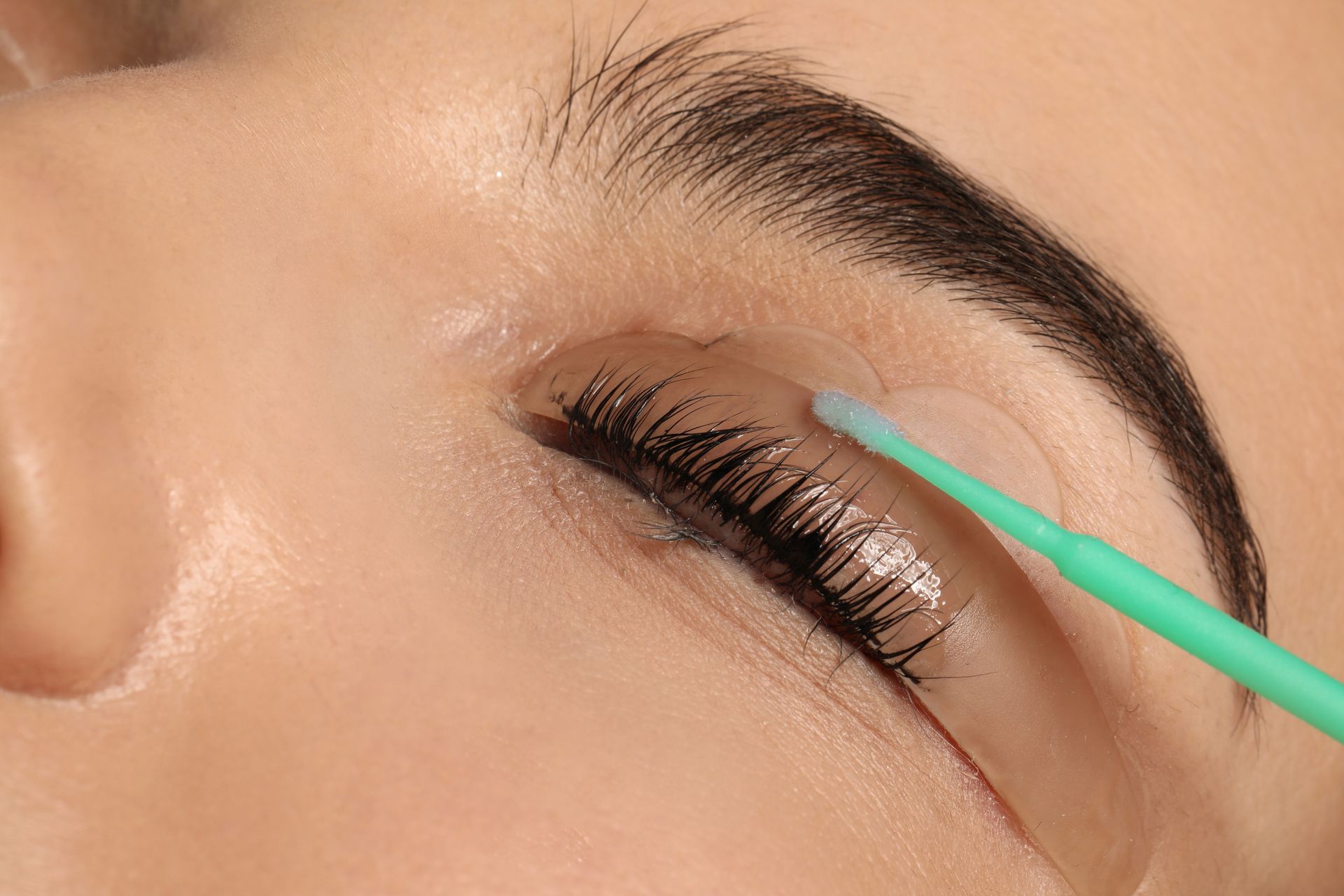 Gros plan sur un œil pendant qu'un applicateur turquoise applique du mascara sur des cils recourbés.
