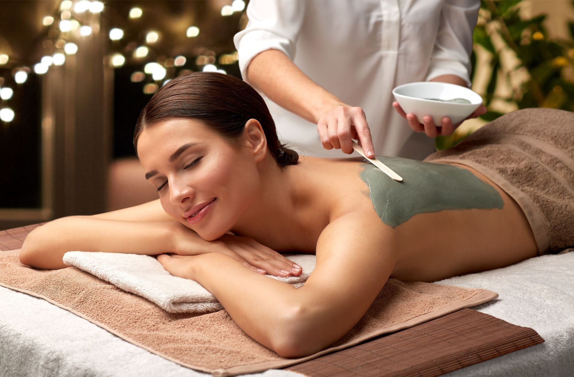 Une esthéticienne applique un masque facial vert à une femme allongée sur une table de massage.