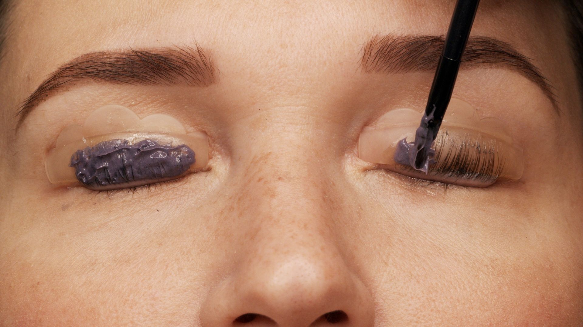 Gros plan sur des yeux fermés, avec application d'un fard à paupières violet foncé au pinceau.