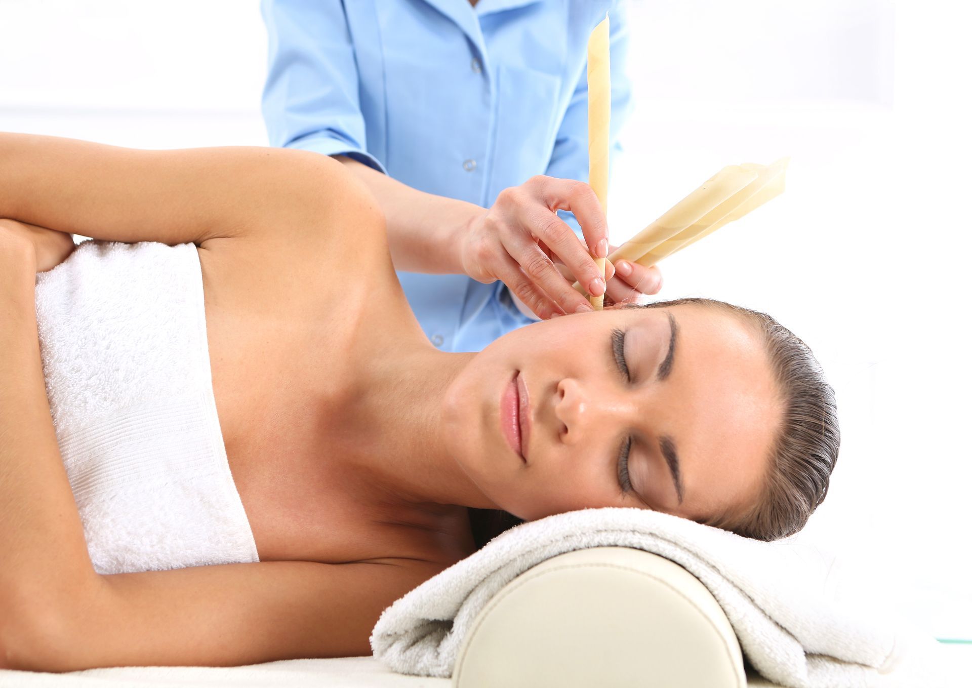 Une femme se fait nettoyer les oreilles à la bougie auriculaire allongée sur une table de massage blanche.